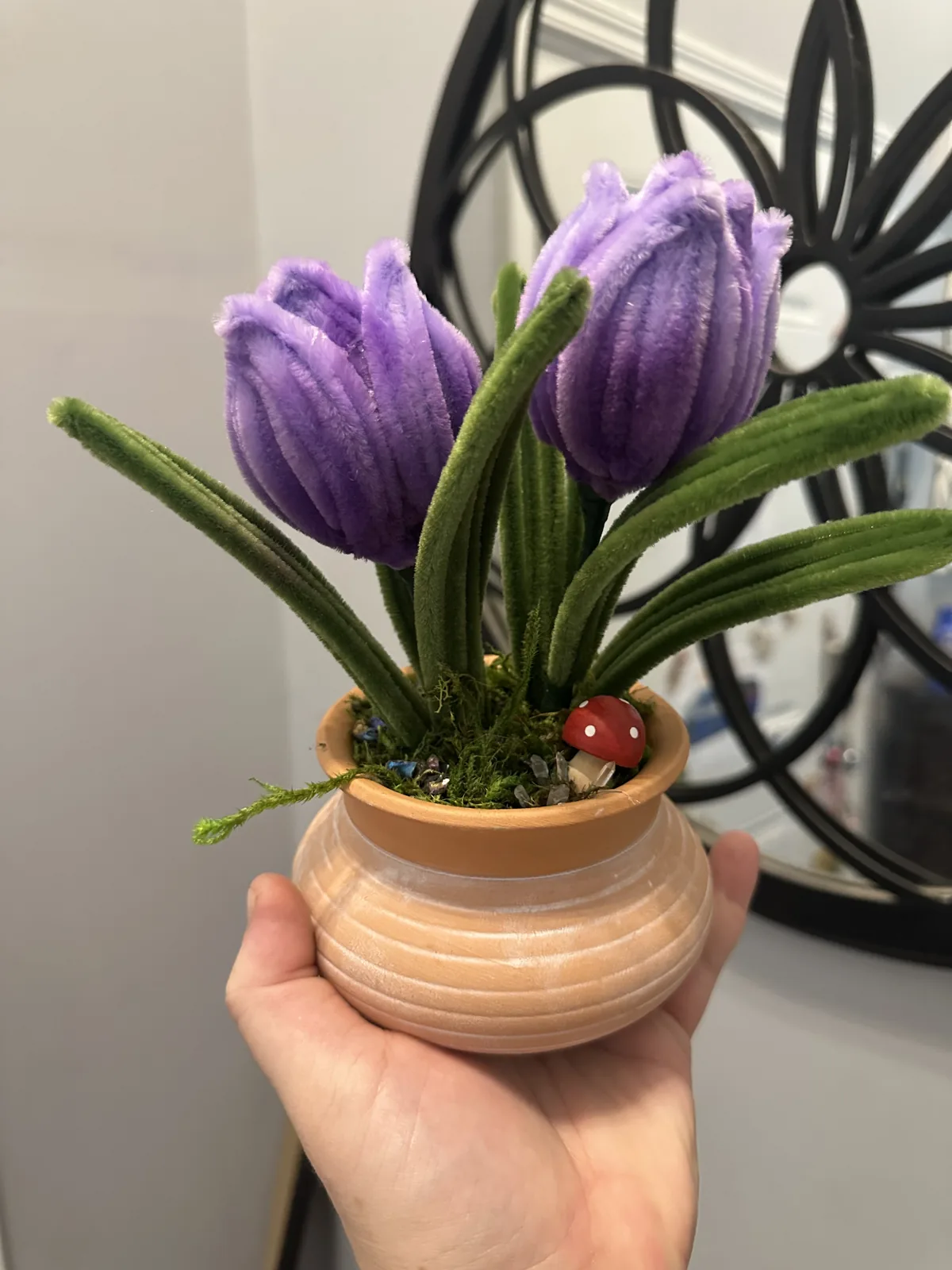 Two purple wire tulips in a peach ceramic pot with moss and a tiny red mushroom